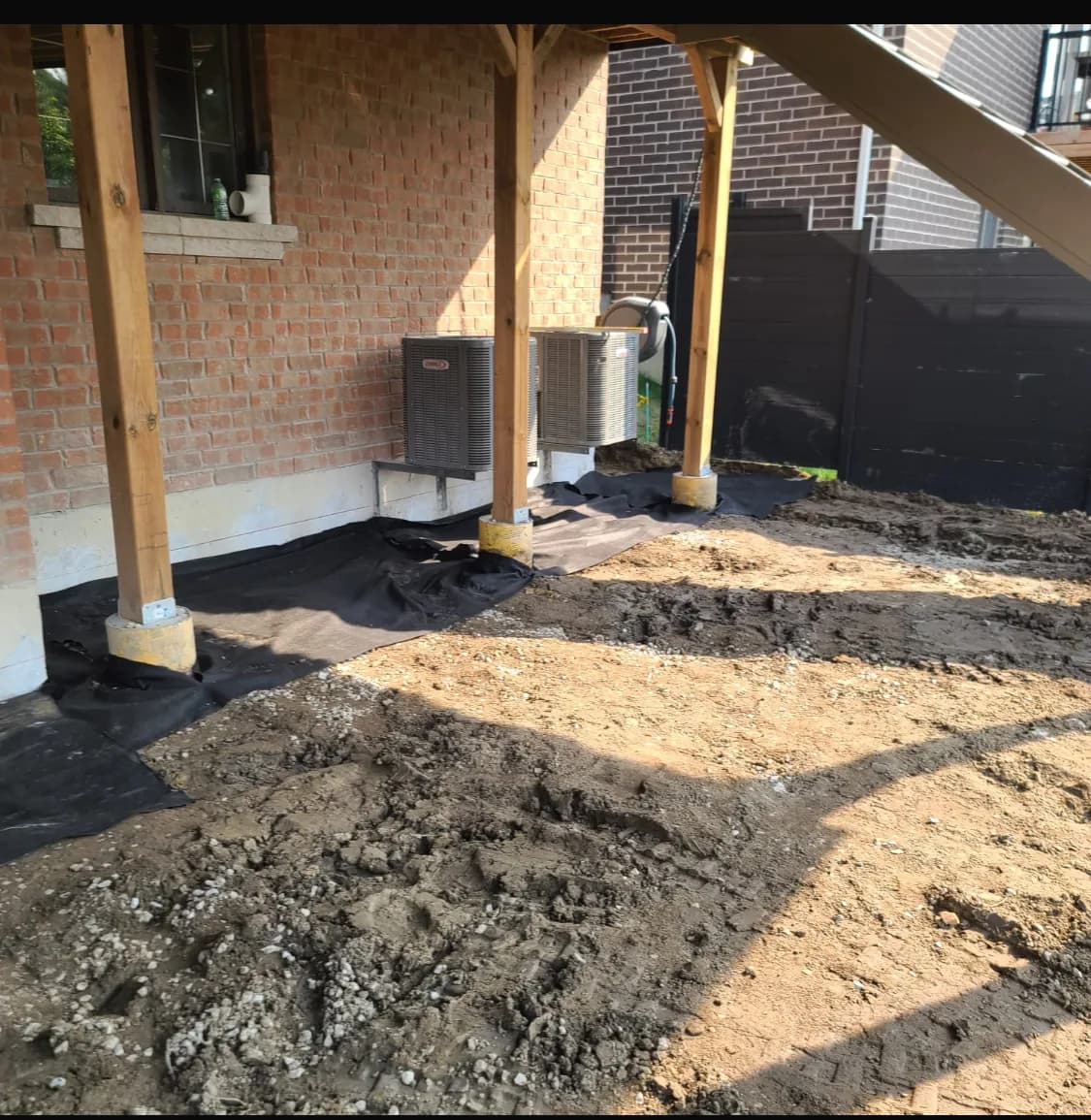 Backyard before hardscaping with stripped soil, geotextile, and bare grade under a covered structure