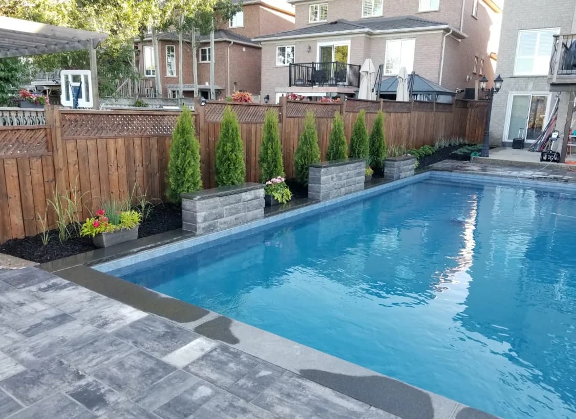 Pool after hardscaping with a finished paver surround, coping, and planted beds