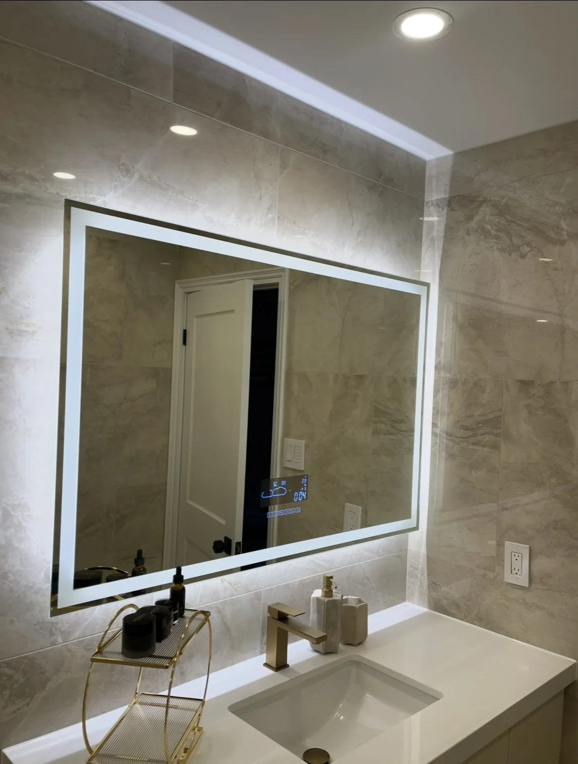 Finished bathroom vanity with illuminated mirror, stone-look wall tile, and gold faucet