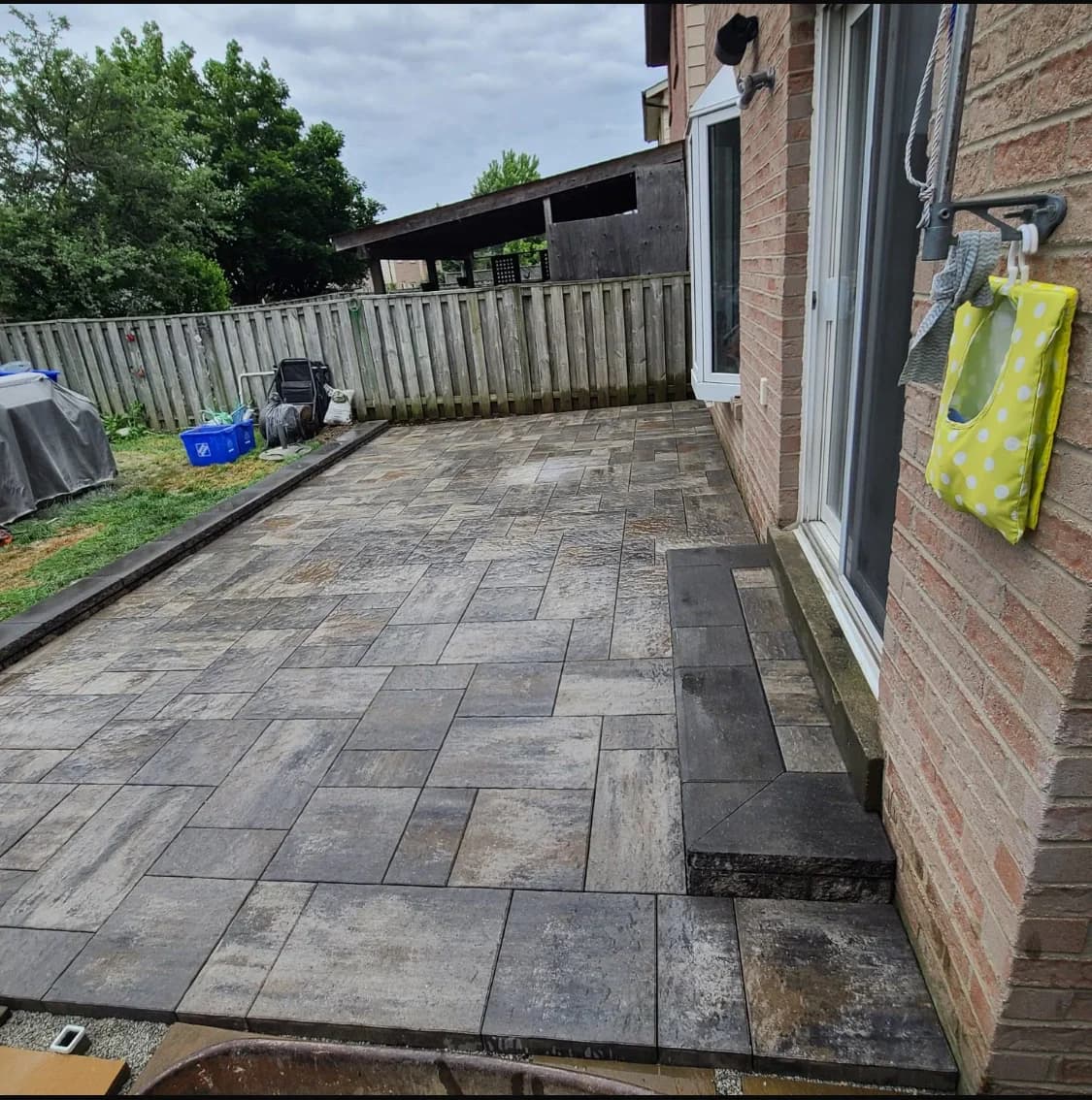 Backyard hardscaping project with large-format paver patio beside a brick home