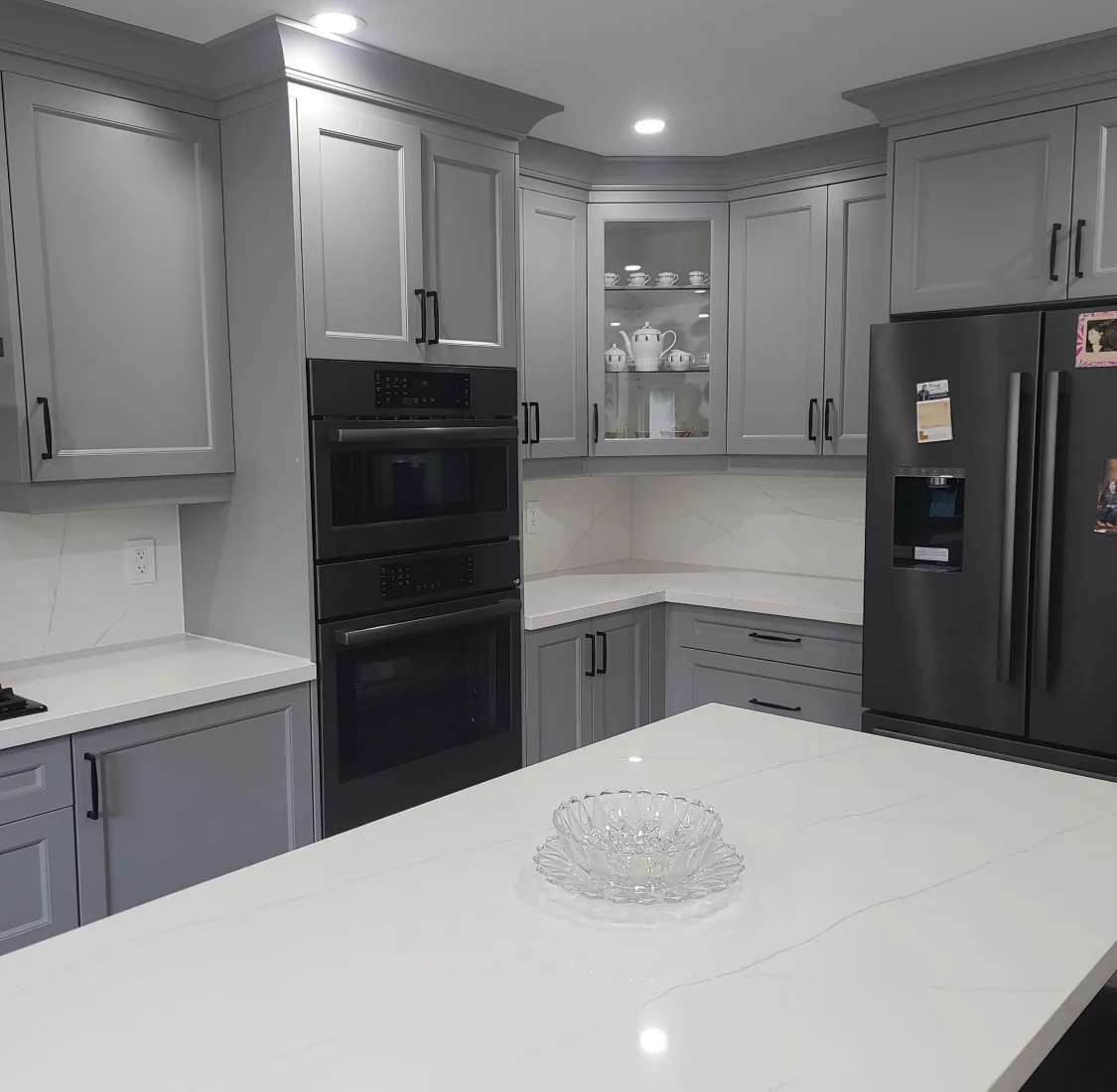 Kitchen renovation with grey cabinets, white counters, black hardware, and built-in appliances