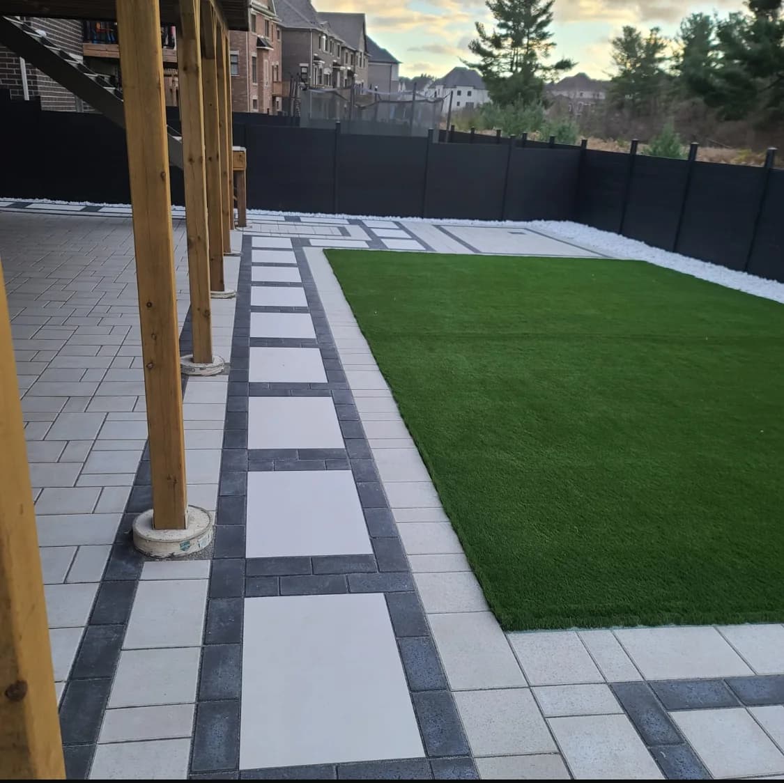 Backyard landscaping with artificial turf, paver borders, and white stone accents